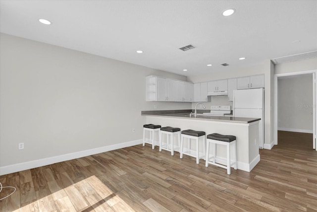 kitchen with white appliances, visible vents, wood finished floors, a peninsula, and white cabinetry