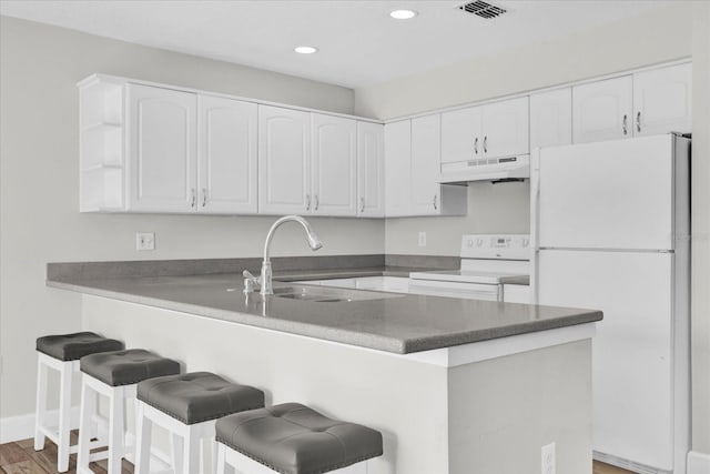 kitchen with dark countertops, white appliances, white cabinets, and under cabinet range hood