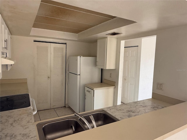 kitchen featuring range hood, a raised ceiling, freestanding refrigerator, white cabinetry, and a sink