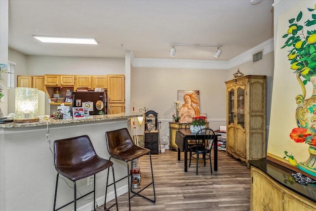 kitchen with a breakfast bar area, wood finished floors, light stone countertops, crown molding, and fridge