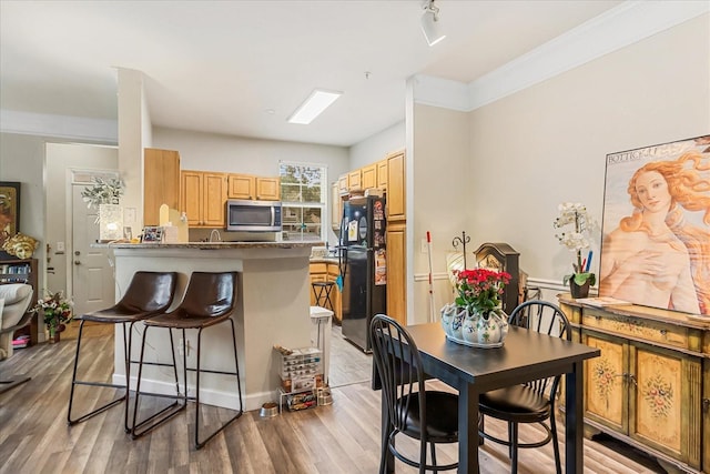 kitchen featuring a breakfast bar, stainless steel microwave, freestanding refrigerator, wood finished floors, and a peninsula