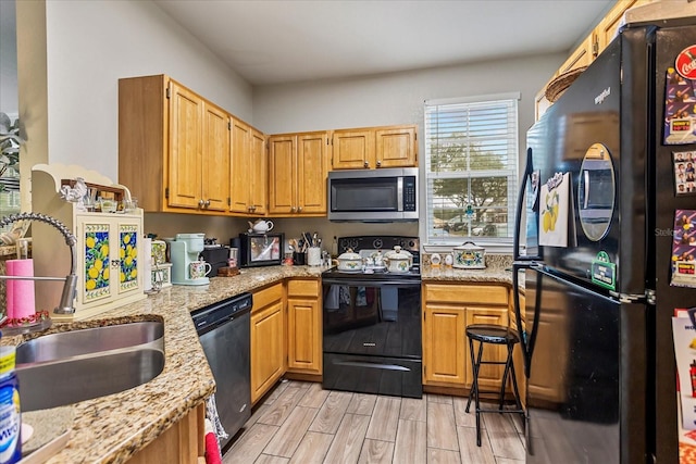 kitchen with black appliances, light stone counters, wood finish floors, and a sink