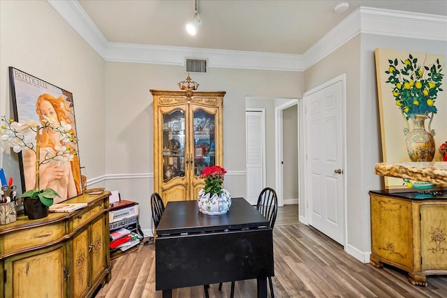 dining space featuring baseboards, visible vents, wood finished floors, and ornamental molding