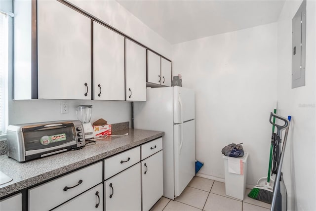 kitchen featuring a toaster, electric panel, freestanding refrigerator, white cabinetry, and light tile patterned flooring