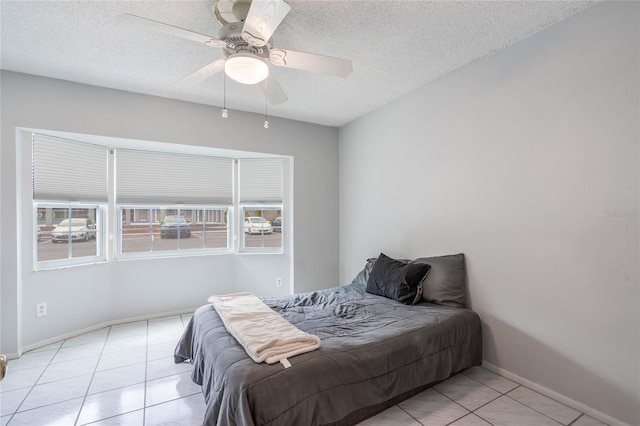 bedroom featuring light tile patterned floors, a ceiling fan, baseboards, and a textured ceiling