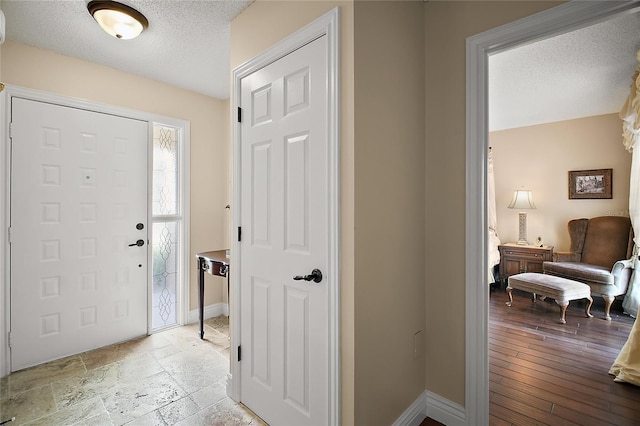 entrance foyer featuring a textured ceiling, stone tile floors, and baseboards