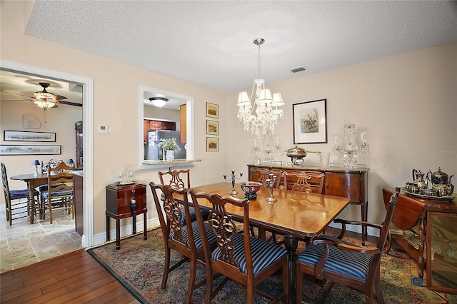 dining room featuring baseboards, visible vents, wood finished floors, a textured ceiling, and ceiling fan with notable chandelier