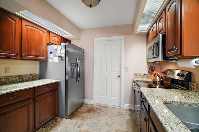 kitchen with appliances with stainless steel finishes, stone finish floor, baseboards, and light stone countertops