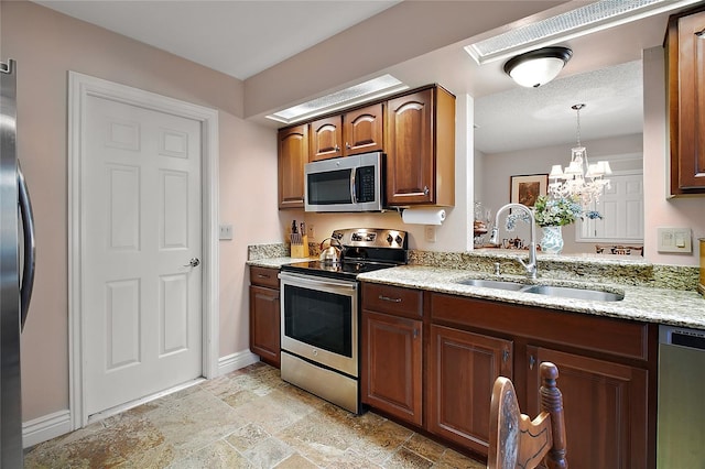 kitchen with stainless steel appliances, light stone counters, hanging light fixtures, and a sink