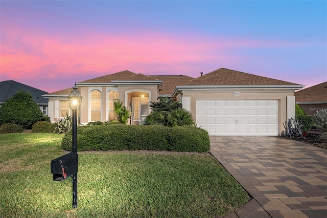 mediterranean / spanish-style house featuring an attached garage, a yard, decorative driveway, and stucco siding