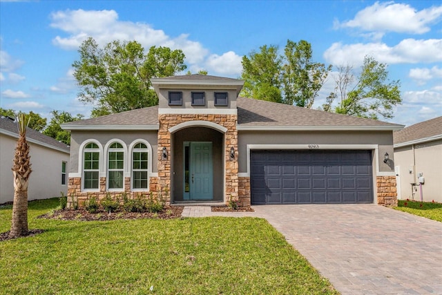 view of front facade with an attached garage, stone siding, a front lawn, and decorative driveway