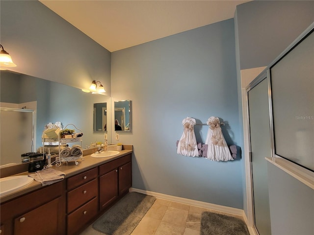 full bathroom featuring double vanity, a shower stall, baseboards, and a sink