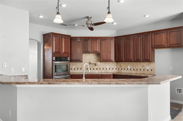 kitchen featuring pendant lighting, light countertops, ceiling fan, and a peninsula