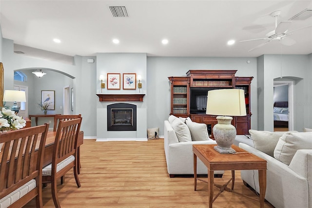 living area with light wood finished floors, visible vents, a fireplace, and arched walkways