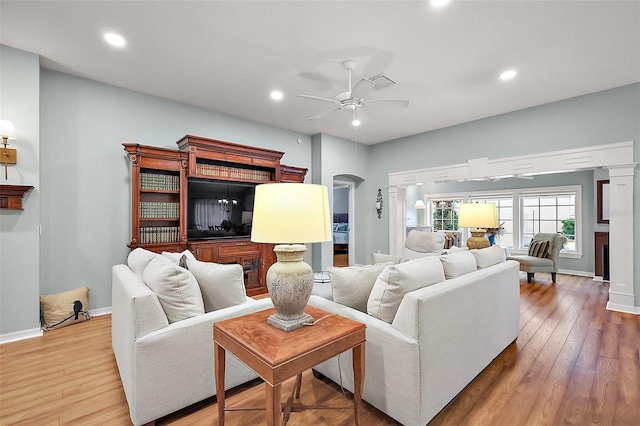 living room featuring baseboards, arched walkways, a ceiling fan, wood-type flooring, and a fireplace