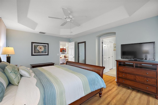 bedroom featuring light wood-type flooring, a tray ceiling, visible vents, and a ceiling fan