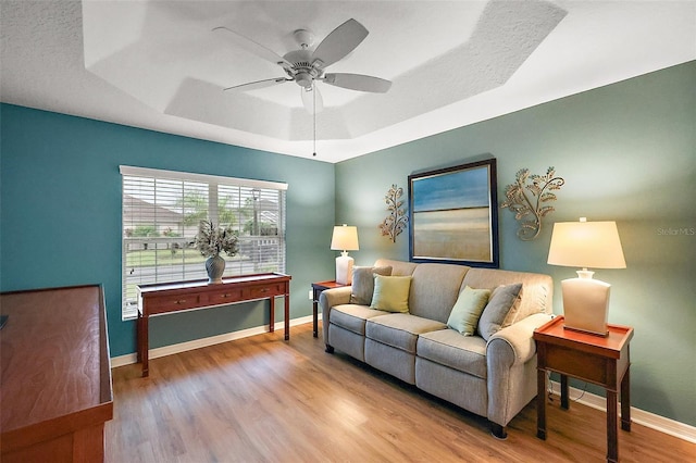 living area featuring a raised ceiling, ceiling fan, baseboards, and wood finished floors