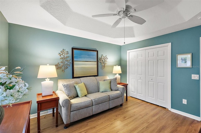 living room with a ceiling fan, a tray ceiling, baseboards, and wood finished floors