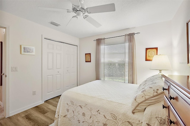 bedroom with baseboards, visible vents, a ceiling fan, wood finished floors, and a closet