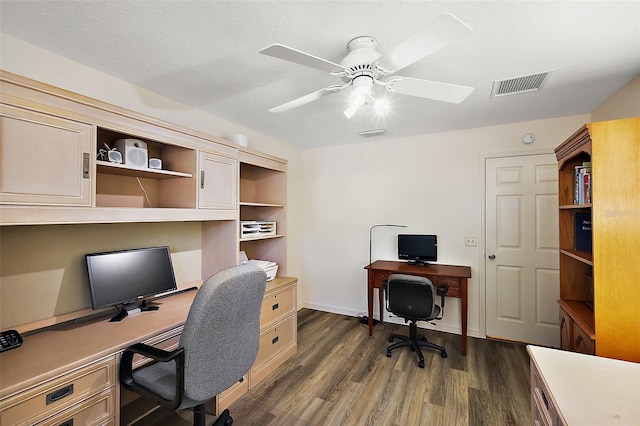 home office featuring dark wood-type flooring, visible vents, a textured ceiling, and a ceiling fan