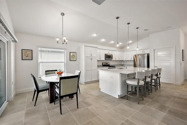 kitchen with a center island with sink, lofted ceiling, appliances with stainless steel finishes, white cabinetry, and a sink