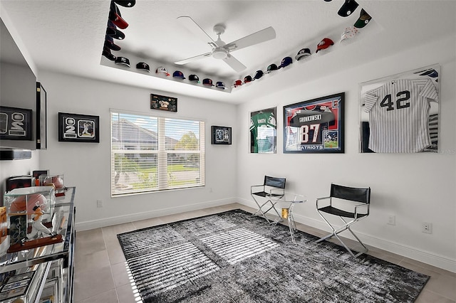 living area with a tray ceiling, a ceiling fan, a textured ceiling, tile patterned flooring, and baseboards