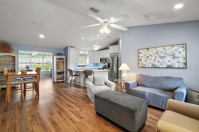 living room featuring a textured ceiling, visible vents, vaulted ceiling, and wood finished floors