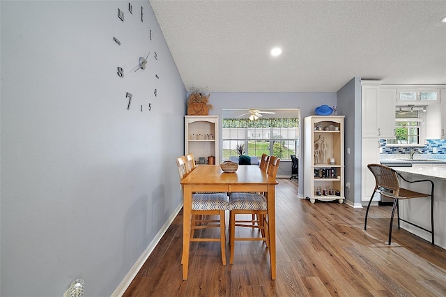 dining room featuring baseboards, a ceiling fan, lofted ceiling, wood finished floors, and a textured ceiling