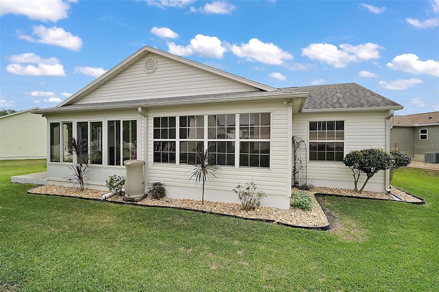 back of house featuring a shingled roof, a sunroom, a lawn, and central AC unit