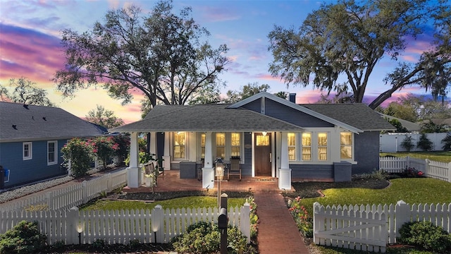 bungalow-style house with covered porch, a shingled roof, a fenced front yard, and a chimney