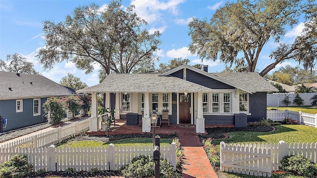 bungalow-style home with a fenced front yard, covered porch, roof with shingles, a chimney, and a front yard