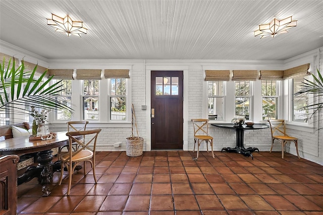 foyer entrance featuring ornamental molding, brick wall, and dark tile patterned flooring