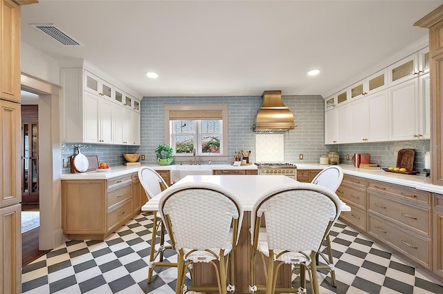 kitchen featuring glass insert cabinets, light countertops, premium range hood, and light floors