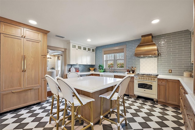 kitchen featuring dark floors, light countertops, custom range hood, glass insert cabinets, and gas range