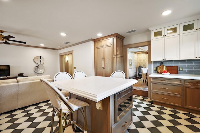 kitchen featuring dark floors, light countertops, glass insert cabinets, a kitchen island, and a kitchen breakfast bar