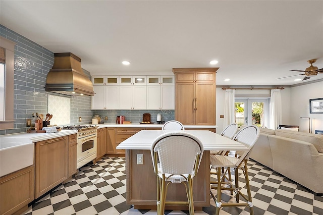 kitchen with island range hood, range with gas cooktop, glass insert cabinets, light countertops, and light floors