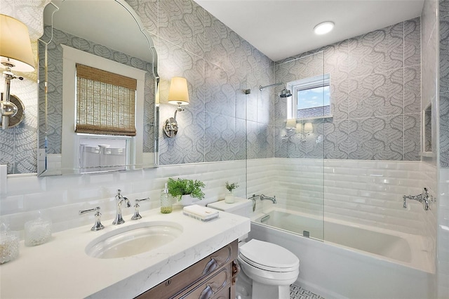 full bath with wallpapered walls, toilet, vanity, washtub / shower combination, and tile walls