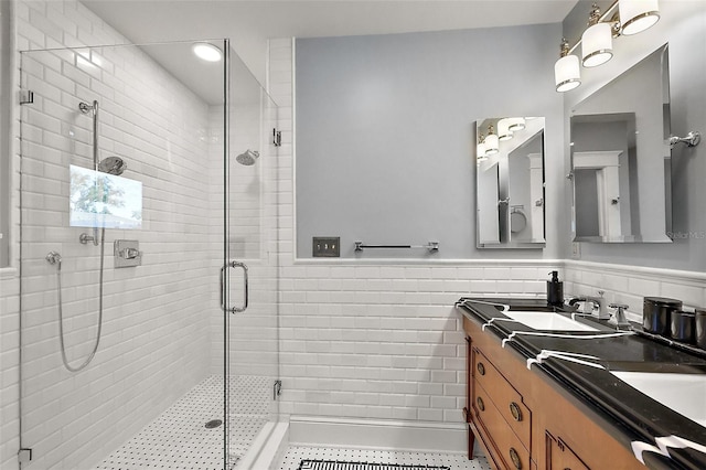 full bathroom featuring double vanity, a wainscoted wall, a sink, a shower stall, and tile walls