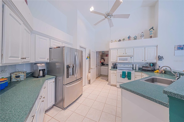 kitchen with white appliances, light tile patterned floors, dark countertops, white cabinetry, and a sink