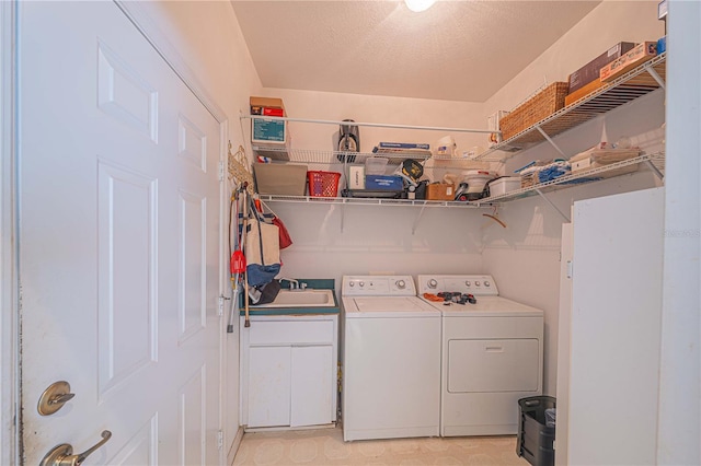 washroom featuring a sink, a textured ceiling, washing machine and clothes dryer, and cabinet space