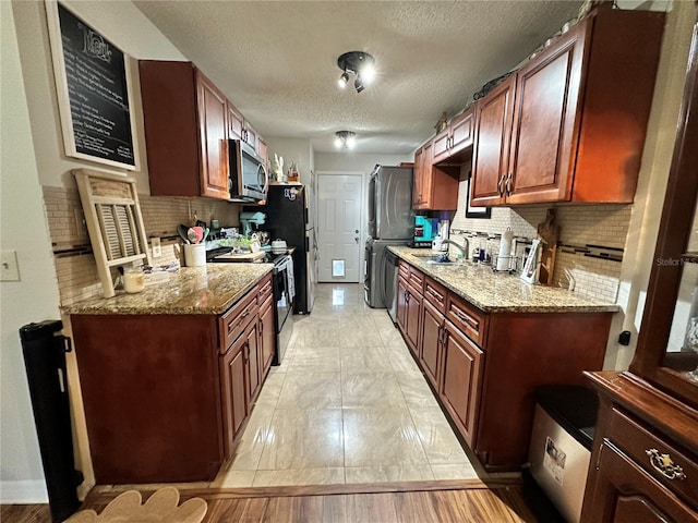 kitchen with appliances with stainless steel finishes, a textured ceiling, decorative backsplash, and light stone countertops