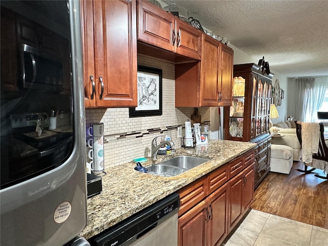 kitchen with a textured ceiling, light stone counters, stainless steel appliances, a sink, and decorative backsplash