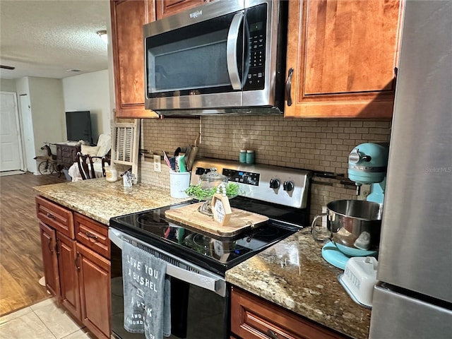 kitchen with decorative backsplash, light stone counters, stainless steel appliances, and a textured ceiling