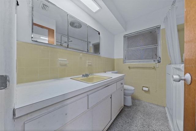 bathroom featuring toilet, a wainscoted wall, visible vents, vanity, and tile walls