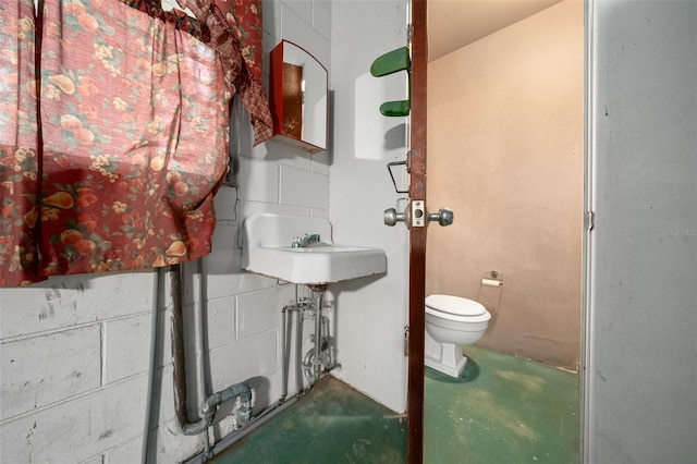 bathroom featuring concrete floors, a sink, concrete block wall, and toilet