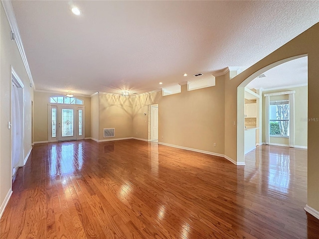 unfurnished living room featuring hardwood / wood-style flooring, baseboards, arched walkways, and crown molding