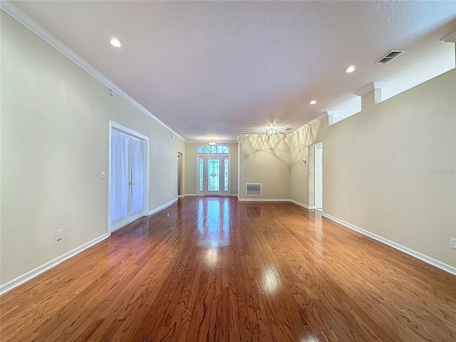 unfurnished living room with a textured ceiling, ornamental molding, wood-type flooring, and visible vents