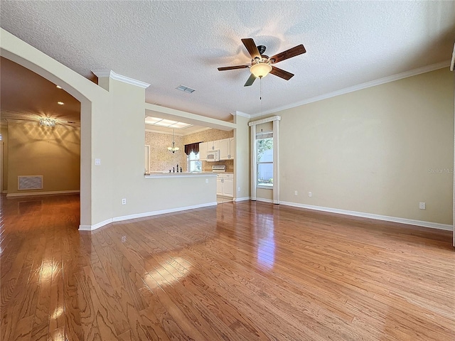 unfurnished living room with arched walkways, ceiling fan, wood finished floors, and visible vents