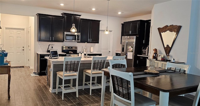 1723 Happiness Row, Kissimmee, FL 34744 - kitchen featuring an island with sink, decorative light fixtures, stainless steel appliances, dark cabinetry, and light countertops