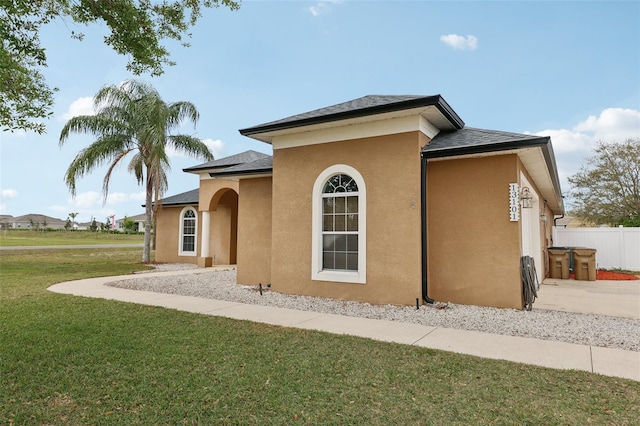 back of property with a shingled roof, a lawn, fence, and stucco siding